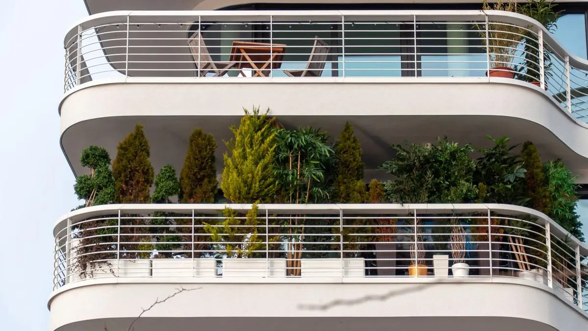 Curved apartment balcony with railing planters full of green plants and outdoor chairs