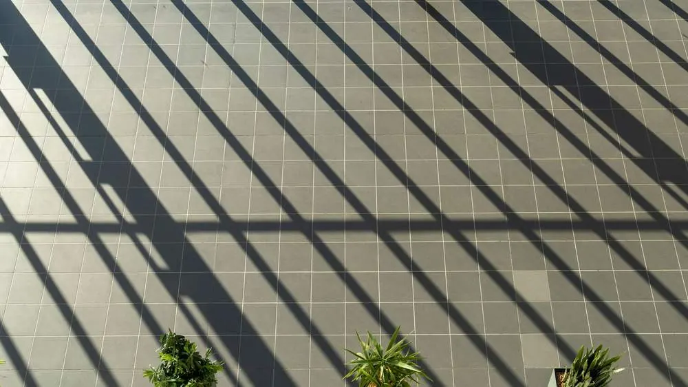 Tiled balcony floor with small potted plants and strong sunlight and shadow lines