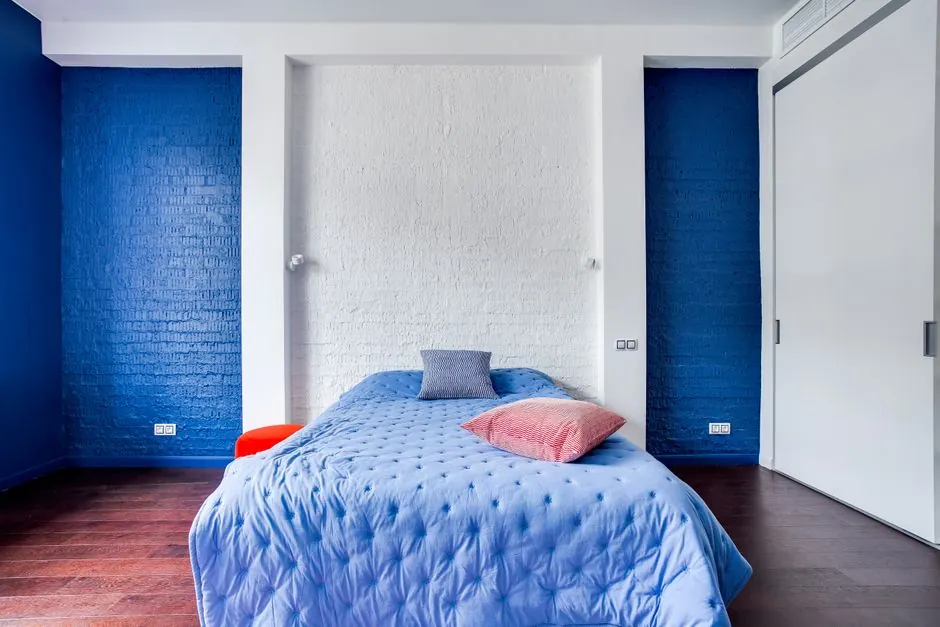 Bedroom with a blue accent wall behind the bed and wooden flooring