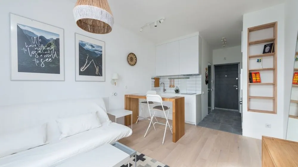 White sofa with cushions in a compact studio living space with an open kitchen beyond