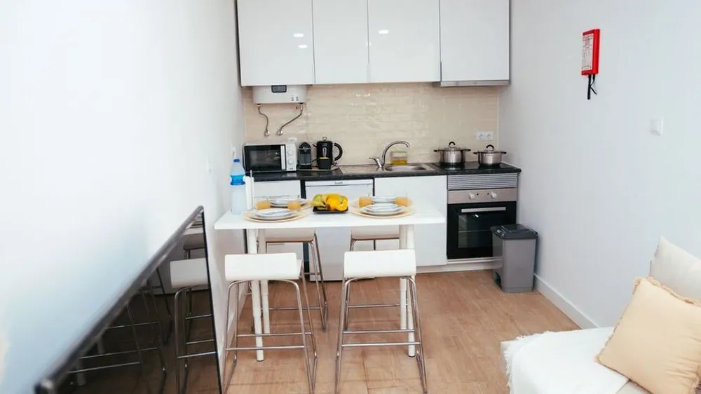 Compact white table with two stools tucked beside a small kitchen in a one-room apartment