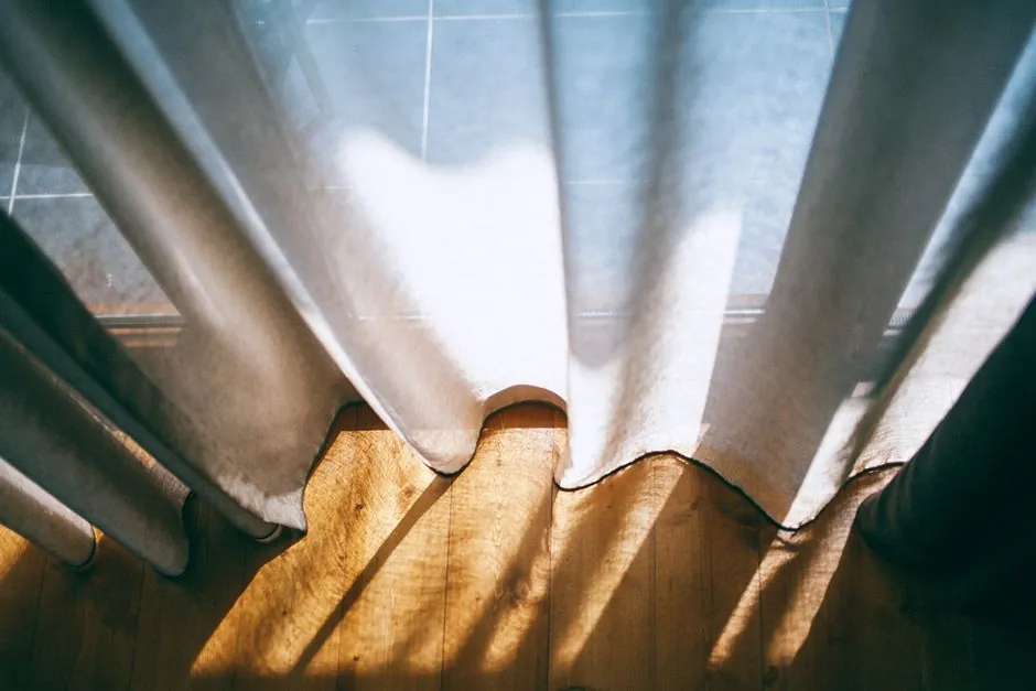Sheer linen curtain falling to a wooden floor in afternoon sun