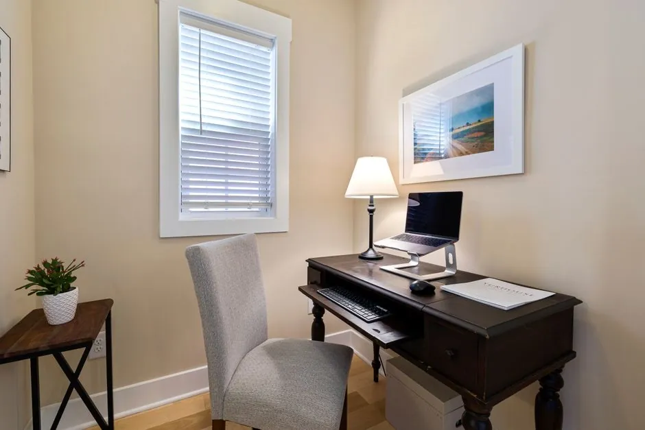 Compact home office desk with a table lamp and laptop stand beside a window
