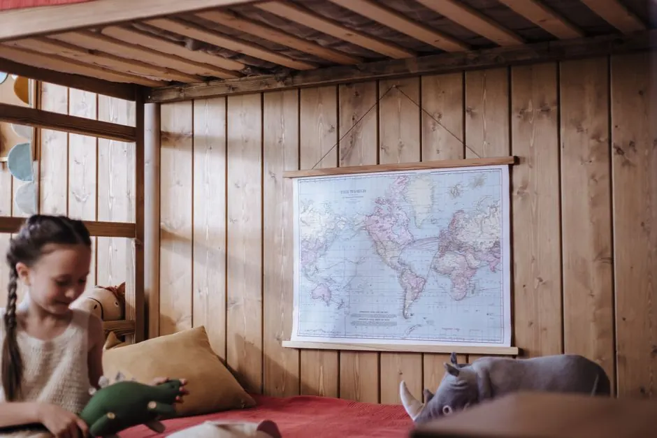 Girl playing on a wooden bunk bed with a world map on the wall