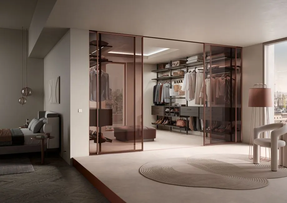 Walk-in wardrobe behind glass sliding doors next to a bedroom